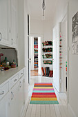 Narrow hallway with white fitted cupboard and multi-coloured rug on white wooden floor