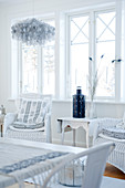 weiße Rattan Stühle mit Kissen neben Beistelltisch am Fenster eines Wohnzimmers in skandinavischem Stil