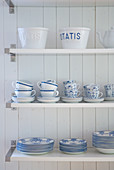 Shelves of white crockery with blue patterns on white, wooden wall