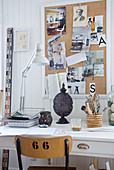 Schreibtisch mit Schreibtischlampe vor Pinnwand an weisser Holzwand