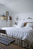 Double bed with linen bed covers in bedroom with rustic wooden bench and white hook rack on wall