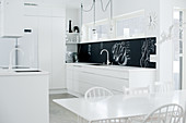 Open-plan designer kitchen in purist white with black splashback