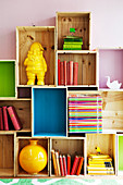 Books and ornaments on DIY shelving made from stacked transport crates, some brightly painted