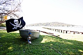 Rowing boot with skull and crossbones flag on grass of lake shore