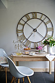 Wooden table, white shell chairs and large wall clock in kitchen