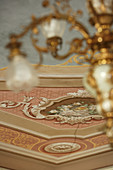 View from below of gold chandelier and painted wall with stucco elements