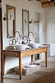 Zwei Waschschüsseln auf rustikalem Holztisch und improvisierte Wandarmaturen unter Wandspiegel im Vintagelook
