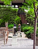 Wooden terrace with lanterns on pedestals in front of a garden and wall covered with green plants