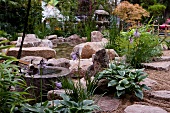 Large stones and grasses on edge of garden pond with Japanese lamp in background