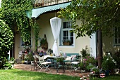Terrassenplatz mit leichten Gartenmöbeln im Shabby-Look vor altem Landhaus mit Sommergarten