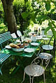 Gedeckte Tische und zusammengewürfelte Stühle unter einem Baum für ein idyllisches Essen im Garten