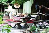Rustic seating area with wooden benches, wooden table and cushions in front of stable