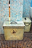 Vintage metal storage box in bathroom against pale blue wall tiles and on dark brown mosaic floor tiles