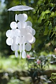 Delicate wind chimes made from white mother-of-pearl discs hanging in garden