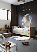 Eclectic child's bedroom- vintage bed against dark wall with space motif and soft toys on chair and floor