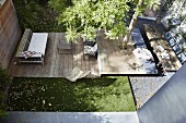 Strip-shaped terrace on several levels with tree growing through deck in sunny urban garden