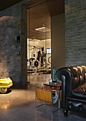 Black vintage leather armchair and magazine rack in front of brick wall with view of gym through glass door