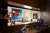 Kitchen counter in half-light in front of open serving hatch with view of picture on blue-painted partition in dining room