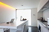 Sink unit with laptop on breakfast bar and stainless steel worksurface on white fitted counter in minimalist designer kitchen