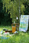 Picnic blanket, cushions, shelving holding water melons and logs and colourful cloth hung as a windbreak