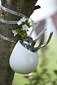 Cutlery in pot hanging on tree trunk