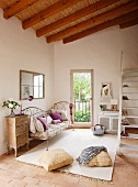 Mediterranean ambiance in simple interior with thatched panels on ceiling; delicate metal couch and vintage chest of drawers combined with pale rug on terracotta floor