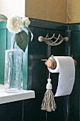 Corner of bathroom with half-height wood-panelling and toilet roll holder next to flower in vase on windowsill