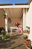 weiße holzverkleidete Loggia mit untergestelltem Tisch und Pflanzentöpfe auf sonniger Terrasse
