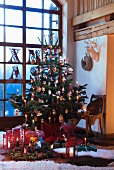 Decorated Christmas tree with lit candles in corner of room in front of floor-to-ceiling lattice window