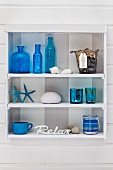 Blue bottles and glass in small, white, shabby-chic shelving unit