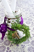 Wreath of conifer twigs tied to jar of candles with ribbon