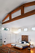 Modernes Schlafzimmer mit Holztragkonstruktion an Decke und afrikanischer Teppichläufer vor Doppelbett