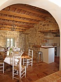 Stone walls and rustic wooden ceiling lend a Mediterranean air to a simple, white kitchen-dining room