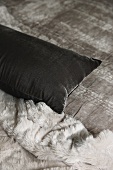 Cushion with grey velvet cover next to fur blanket on bed