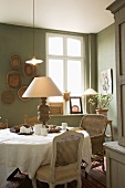 Comfortable dining room with various antique chairs at round table and table lamp with turned wooden base