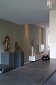 Theke mit grauer Steinplatte in offenem Wohnraum und Skulpturen auf Stele vor grau getönter Wand