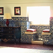 White and blue, half-height tiling on wall and in window niche with window seats next to black and gold Rococo chest of drawers with table lamp