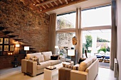 Sofa landscape in a large living room with bank of windows and natural stone and brick wall