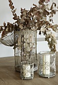 Dried branches of leaves in vintage-style bird cage and white candles in candle lanterns