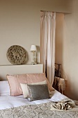 Scatter cushions on bed next to airy curtain in open doorway of simple bedroom