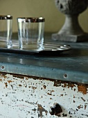 Tray of glasses on vintage chest of drawers with peeling paint and metal-clad top panel