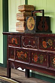 Various wooden boxes on wooden chest of drawers painted with floral motifs against green wall