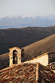 Tiled roof of old Italian church with bell tower and view of mountain landscape
