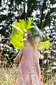 Blond girl holding rhubarb leaf as parasol