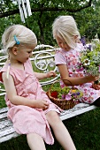 Two blonde girls with flowers sitting on garden bench