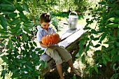 Young boy sitting with a pumpkin on a garden bench
