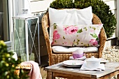 Kaffeepause im Freien - Rattanstuhl mit Kissen und Tassen auf Beistelltisch vor Hauswand
