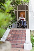 Älterer Mann im Rollstuhl beim Hauseingang