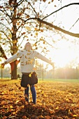 Girl playing with fallen autumn leaves in park
