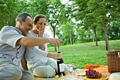 Mature couple having picnic outdoors, opening bottle of wine
